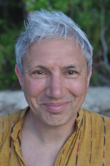 A man with grey hair looking towards the camera with a yellow shirt on.