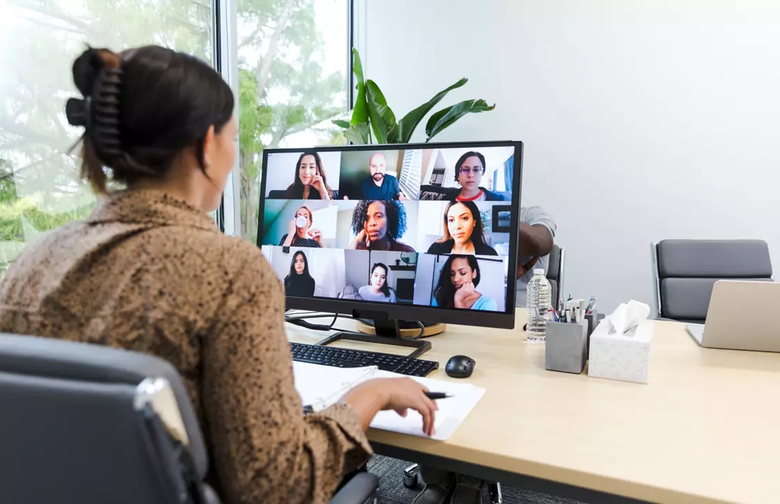 Woman sat at a desk with 9 people on a video call