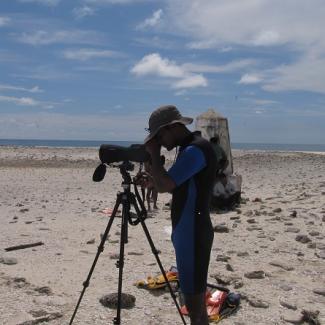 An image of a person on a beach, using a camera and tripod to take photos .